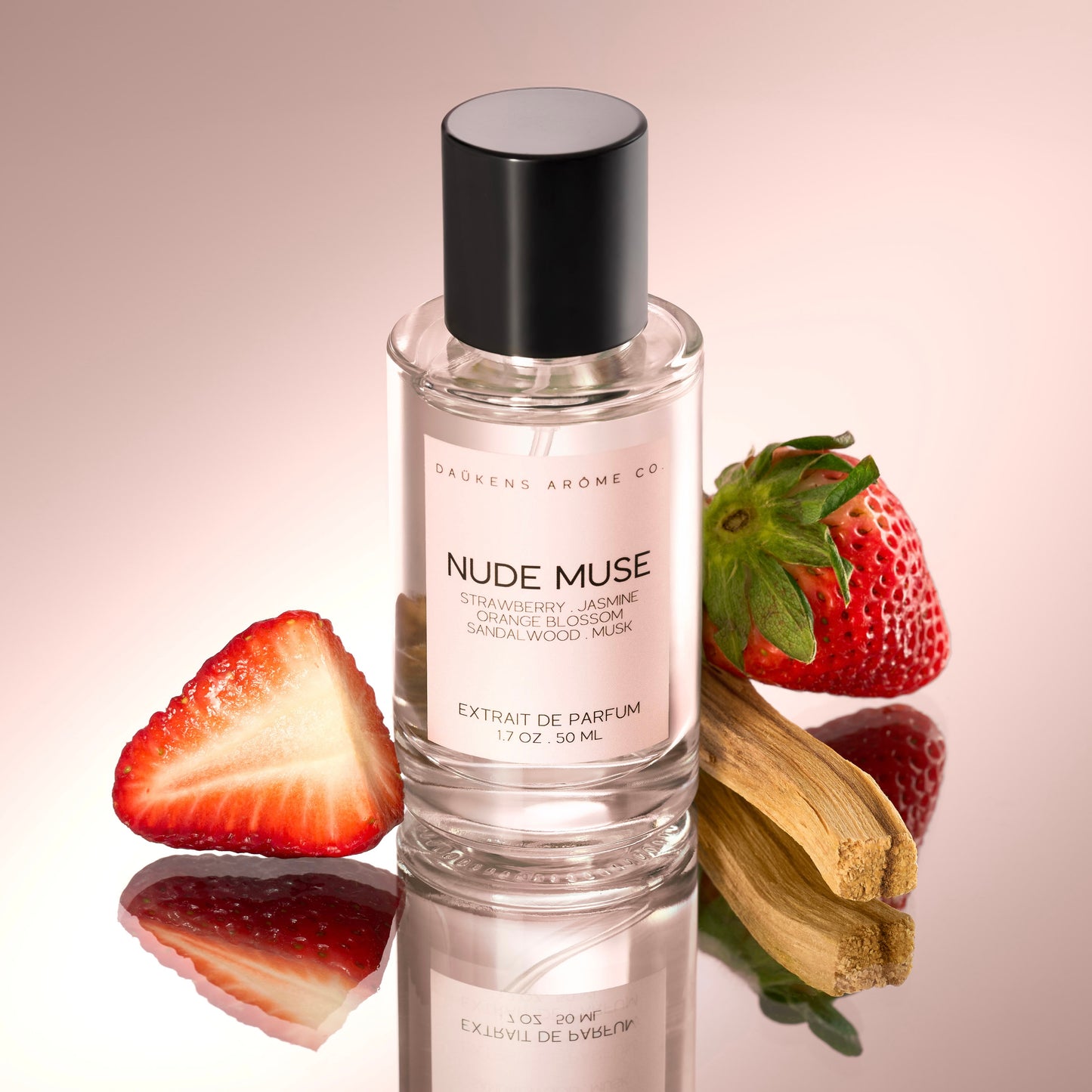 Glass perfume bottle labeled “Nude Muse” by DAÜKENS ARÔME CO., styled with fresh strawberries and vanilla pods on a soft pink background.