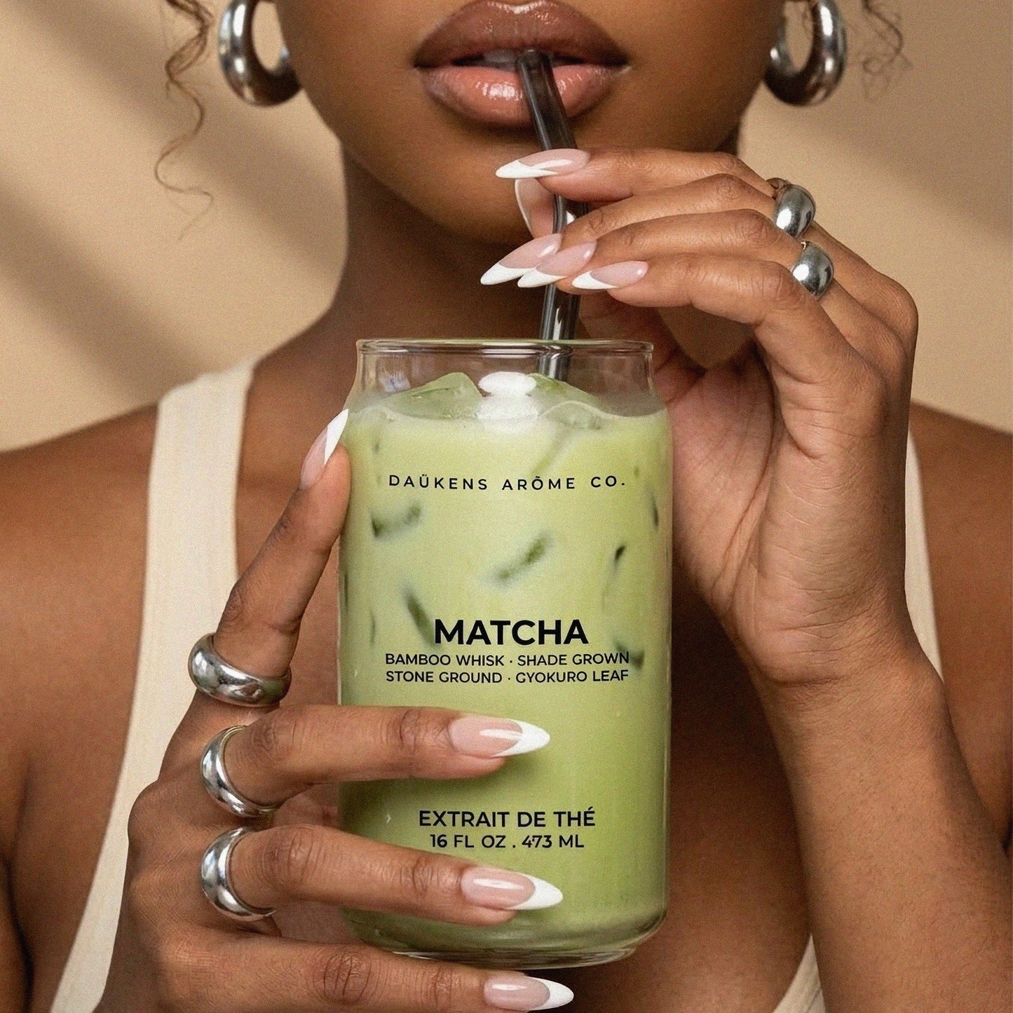 Person holding a glass of matcha drink with Daukens Arome Co. branding.