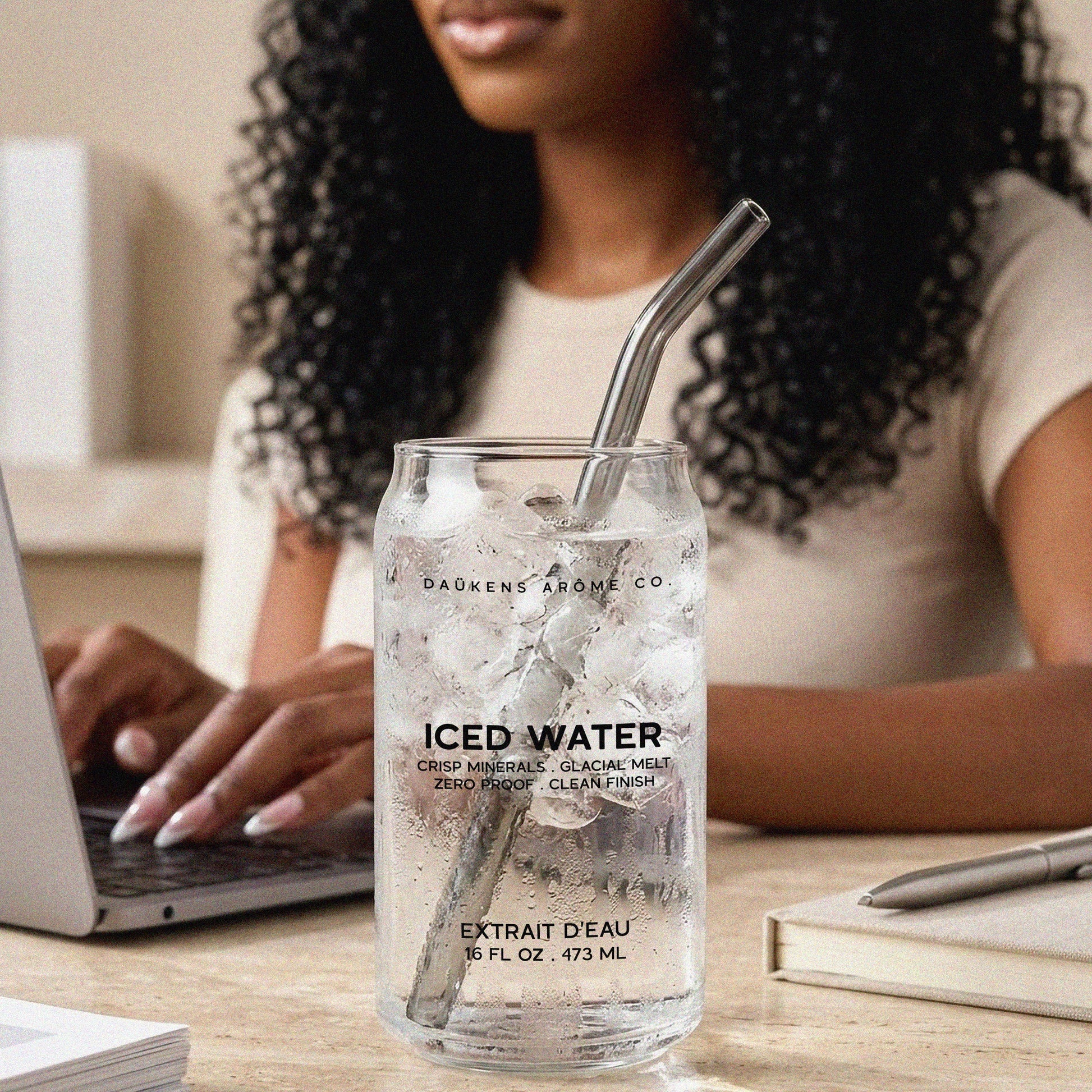Person sitting at a desk with a glass of iced water labeled 'ICED WATER' and 'DAKENS AROMA CO'.