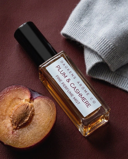 Plum & Cashmere Fine Perfume Mist bottle beside a plum and soft gray fabric.