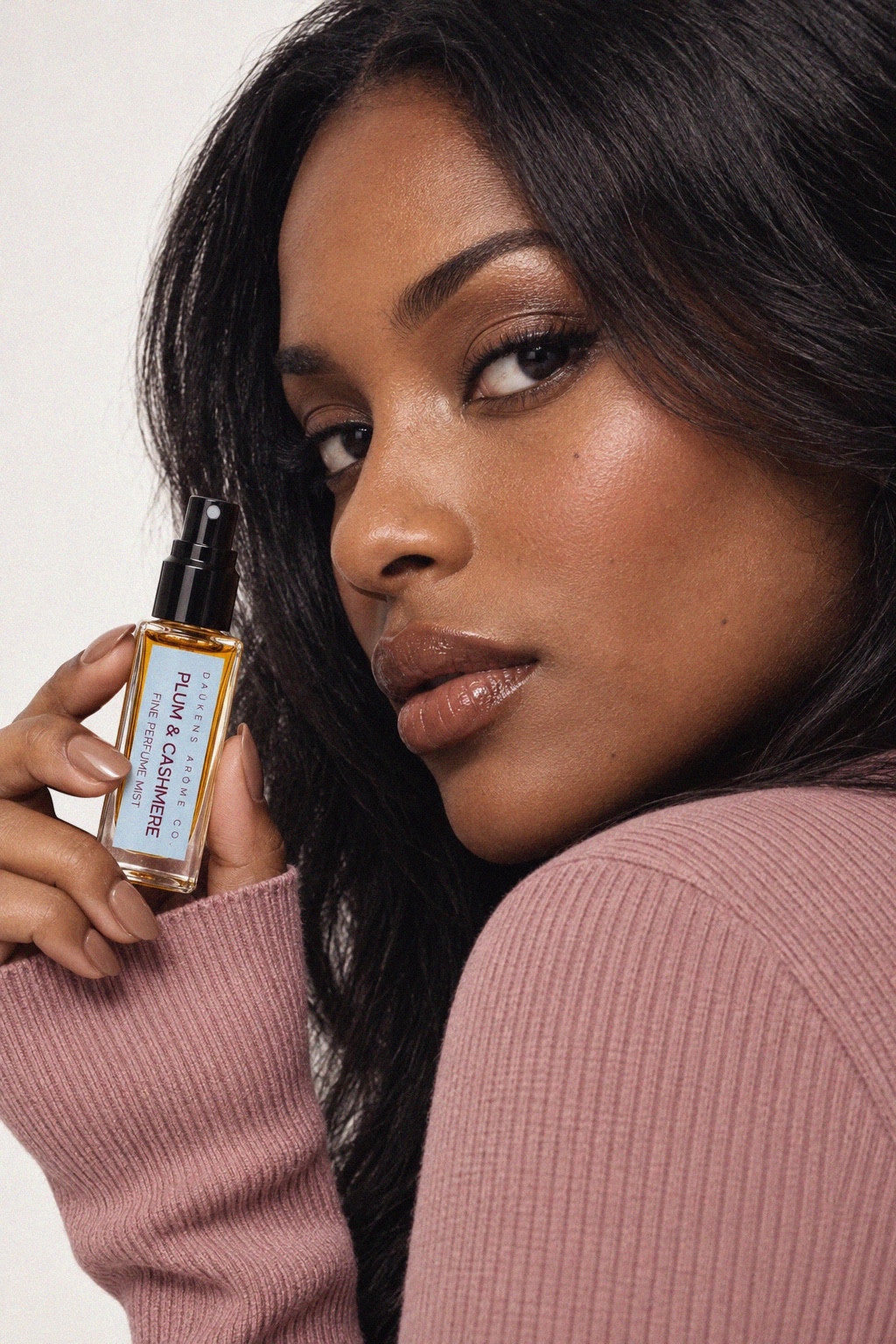 Model in a mauve knit sweater holding a Plum & Cashmere Fine Perfume Mist bottle.